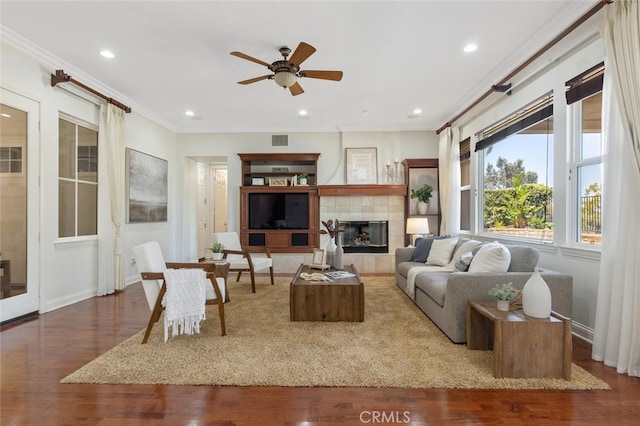 living room with dark wood-type flooring, built in shelves, ornamental molding, ceiling fan, and a fireplace