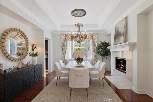 dining area with a notable chandelier, dark wood-type flooring, ornamental molding, and a raised ceiling