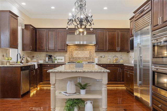 kitchen featuring appliances with stainless steel finishes, a kitchen island, decorative light fixtures, tasteful backsplash, and exhaust hood