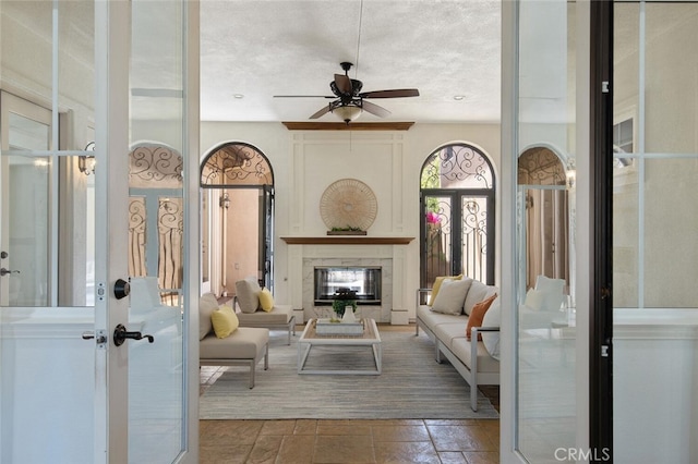 living room with french doors, ceiling fan, and a textured ceiling