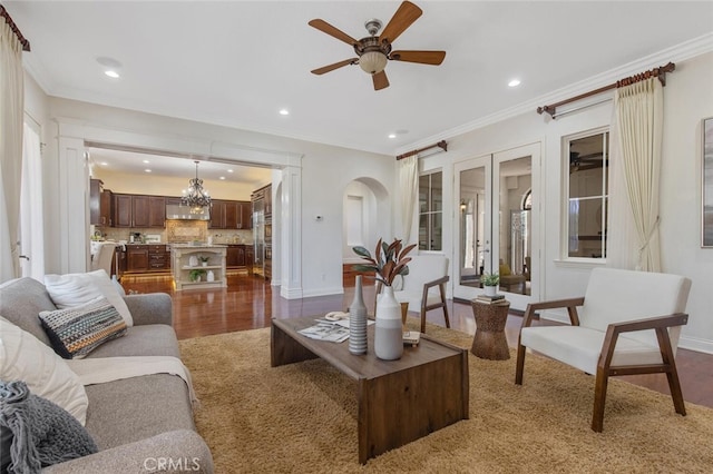 living room featuring crown molding, dark wood-type flooring, and ceiling fan with notable chandelier