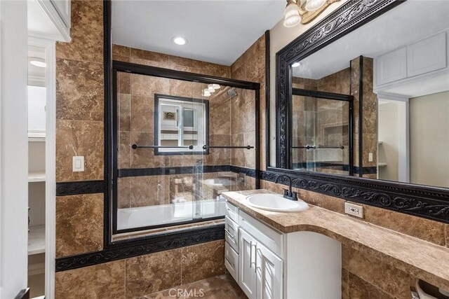 bathroom with shower / bath combination with glass door, vanity, tile walls, and tile floors