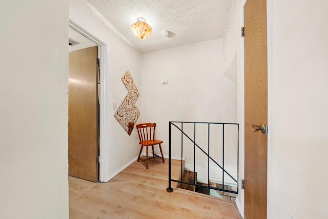 hall with a textured ceiling and light wood-type flooring