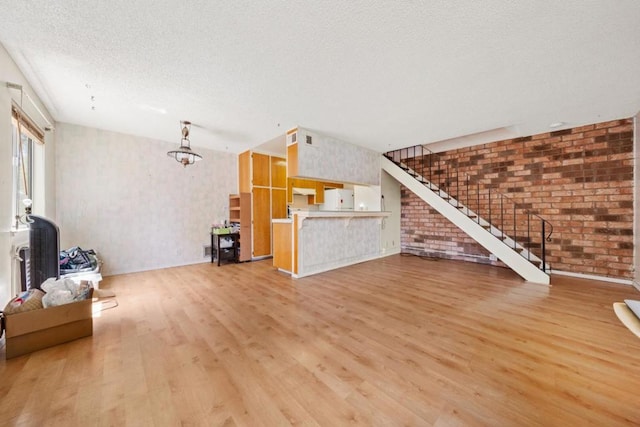 unfurnished living room featuring brick wall, a textured ceiling, and light wood-type flooring