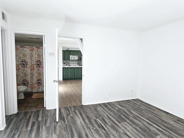 unfurnished bedroom with ensuite bathroom and dark hardwood / wood-style flooring