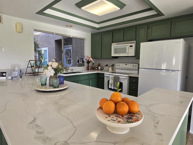 kitchen featuring a raised ceiling, kitchen peninsula, sink, green cabinets, and white appliances