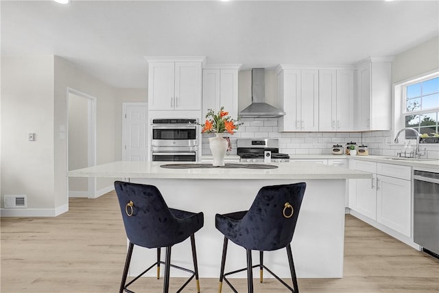 kitchen featuring appliances with stainless steel finishes, white cabinetry, a kitchen island, and wall chimney exhaust hood