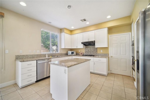 kitchen with white cabinets, stainless steel appliances, a kitchen island, and light stone counters