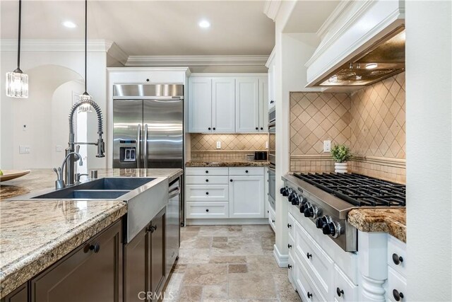 kitchen with light stone countertops, white cabinetry, decorative light fixtures, stainless steel gas stovetop, and custom range hood