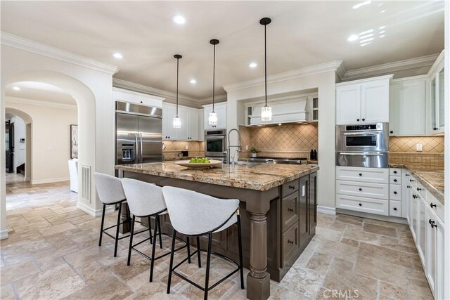 kitchen with a center island with sink, sink, tasteful backsplash, light stone counters, and white cabinetry