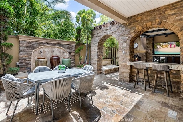 view of patio with outdoor dry bar, outdoor dining space, and an outdoor stone fireplace