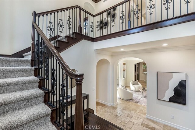 staircase featuring a towering ceiling and crown molding