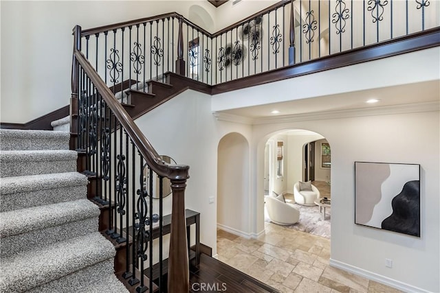 staircase featuring crown molding, arched walkways, baseboards, and stone tile flooring