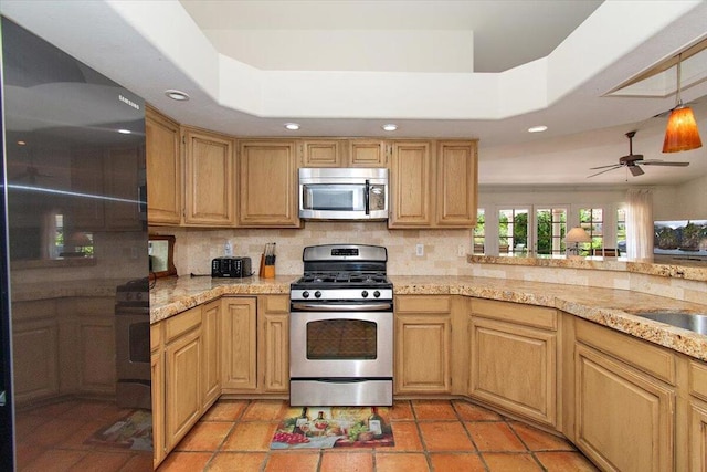 kitchen with ceiling fan, tasteful backsplash, a raised ceiling, light tile floors, and appliances with stainless steel finishes