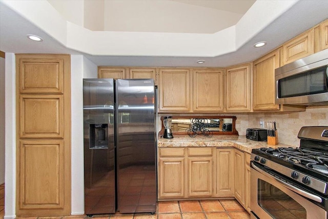 kitchen featuring tasteful backsplash, light tile flooring, a raised ceiling, light stone counters, and appliances with stainless steel finishes