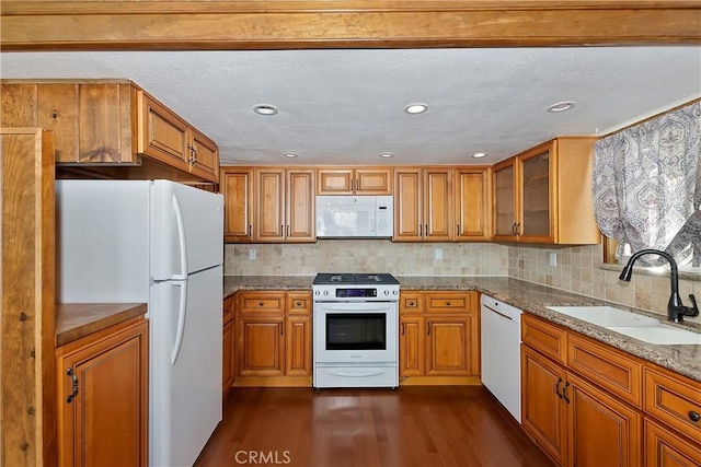 kitchen featuring white appliances, a sink, dark wood-type flooring, glass insert cabinets, and brown cabinets