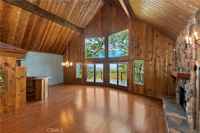 unfurnished living room featuring a stone fireplace, wood-type flooring, an inviting chandelier, and wooden ceiling