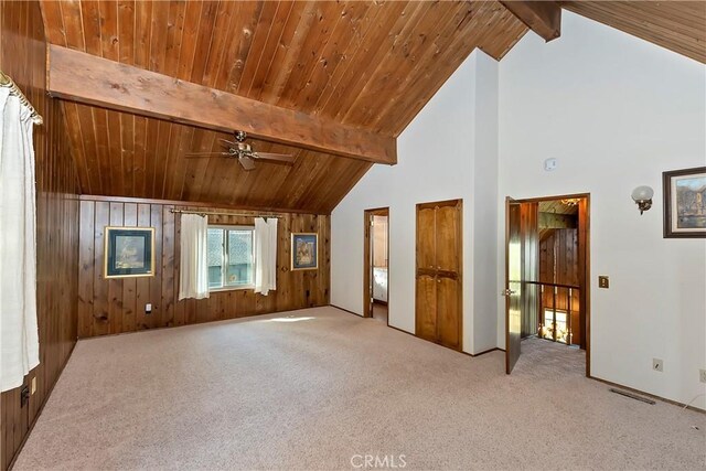 unfurnished living room featuring beam ceiling, ceiling fan, light colored carpet, and wood walls