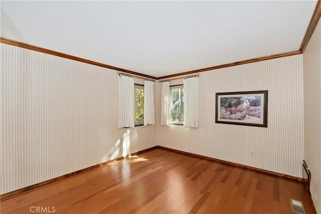 spare room with crown molding, wood finished floors, visible vents, and baseboards