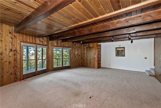 unfurnished living room with beam ceiling, wood walls, stairs, and carpet