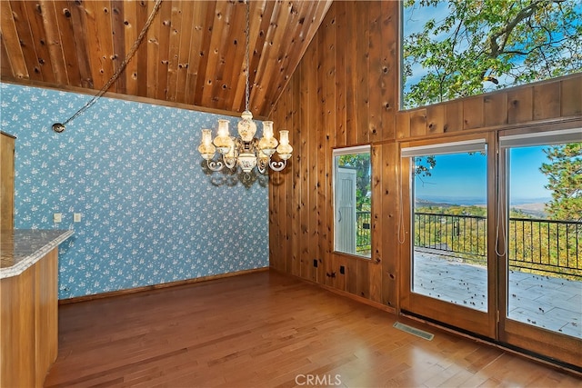 unfurnished dining area featuring a notable chandelier, high vaulted ceiling, and light hardwood / wood-style flooring