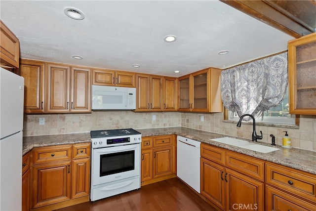 kitchen with white appliances, tasteful backsplash, sink, dark wood-type flooring, and light stone counters