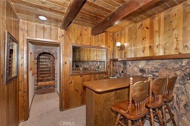 bar featuring beam ceiling, light carpet, wooden ceiling, and wooden walls