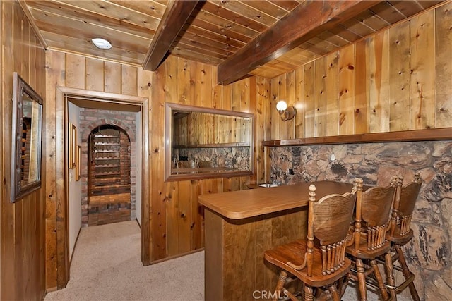 bar with beam ceiling, carpet floors, wooden walls, bar area, and wood ceiling