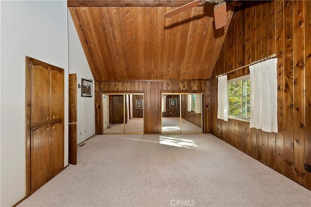 carpeted empty room with wooden ceiling, wooden walls, a ceiling fan, and high vaulted ceiling