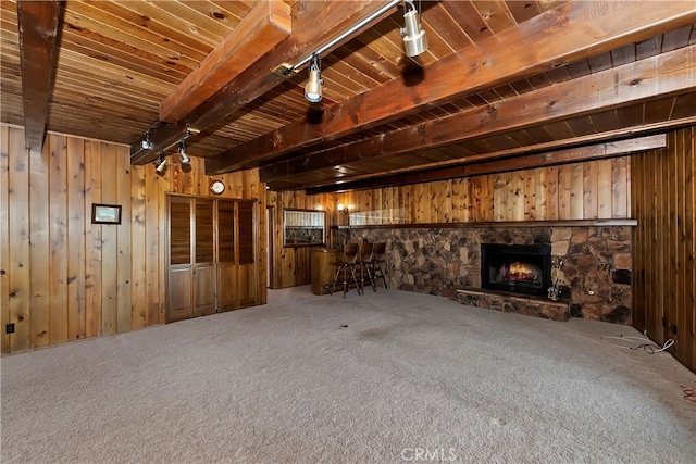 unfurnished living room featuring wood ceiling, beam ceiling, carpet floors, a stone fireplace, and wooden walls