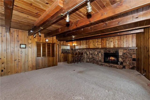 unfurnished living room featuring a stone fireplace, beam ceiling, wooden walls, and carpet flooring