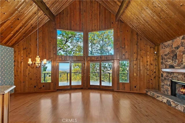 unfurnished living room featuring high vaulted ceiling, wood finished floors, a stone fireplace, wooden ceiling, and a chandelier