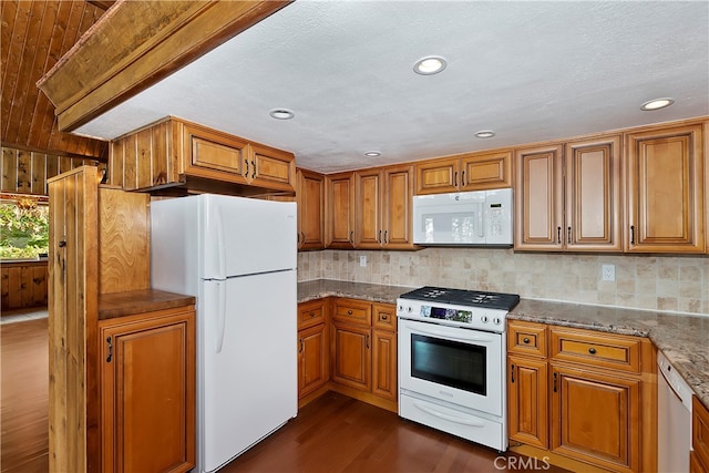 kitchen with wood walls, light stone countertops, tasteful backsplash, white appliances, and dark hardwood / wood-style flooring