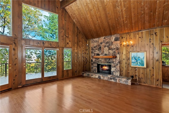 unfurnished living room featuring a stone fireplace, wood walls, hardwood / wood-style floors, and beam ceiling