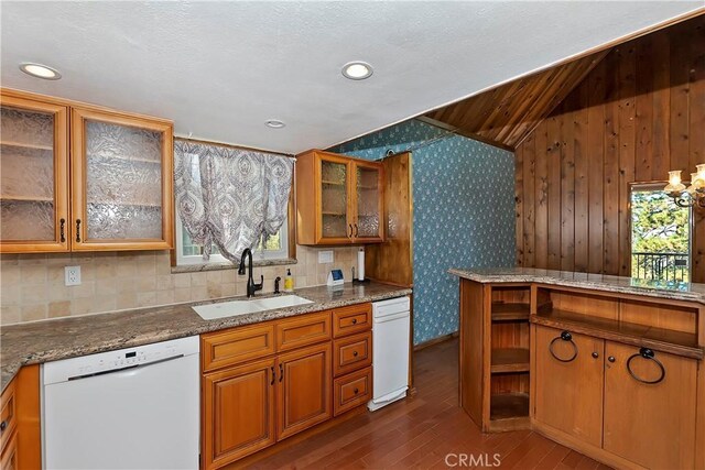 kitchen featuring light stone countertops, wood walls, white dishwasher, and sink