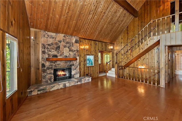 unfurnished living room with a stone fireplace, wooden ceiling, a healthy amount of sunlight, and wood walls