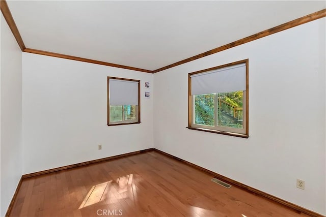 spare room with visible vents, wood-type flooring, baseboards, and ornamental molding