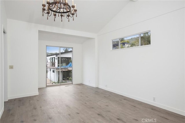 spare room with wood-type flooring, an inviting chandelier, plenty of natural light, and lofted ceiling