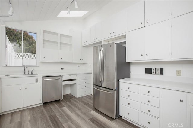 kitchen featuring appliances with stainless steel finishes, rail lighting, lofted ceiling with skylight, sink, and white cabinets