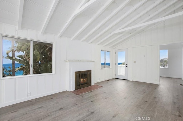 unfurnished living room featuring hardwood / wood-style floors, lofted ceiling with beams, a water view, a fireplace, and plenty of natural light