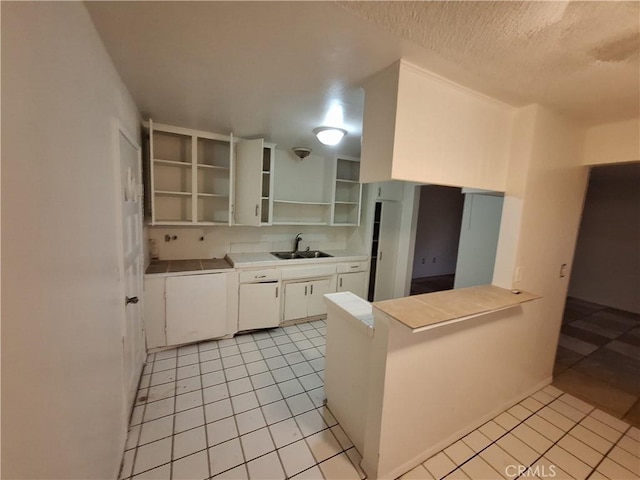 kitchen with white cabinets, sink, light tile patterned floors, a textured ceiling, and kitchen peninsula