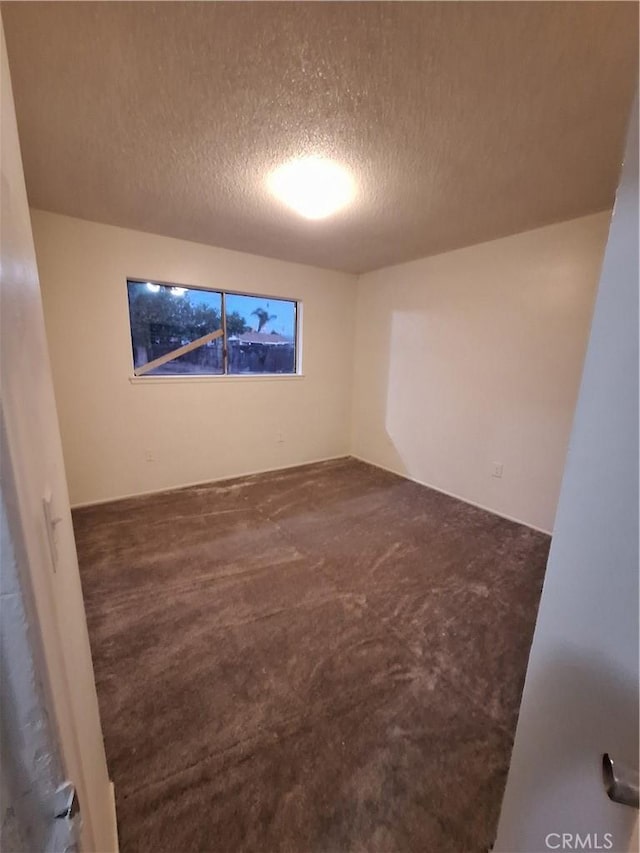 empty room featuring a textured ceiling and dark carpet