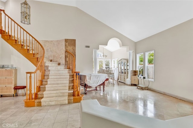 foyer featuring high vaulted ceiling, tile flooring, a notable chandelier, and ornate columns