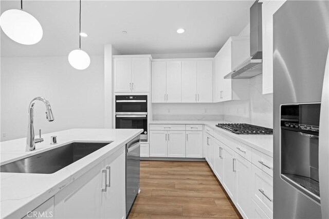 kitchen featuring appliances with stainless steel finishes, white cabinets, wall chimney exhaust hood, sink, and hanging light fixtures