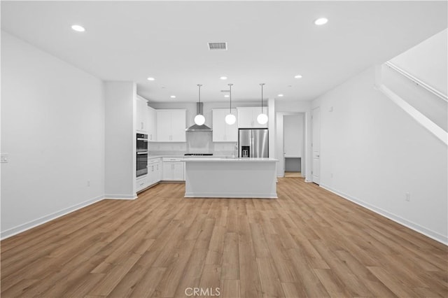 kitchen featuring wall chimney range hood, a kitchen island, white cabinetry, hanging light fixtures, and appliances with stainless steel finishes