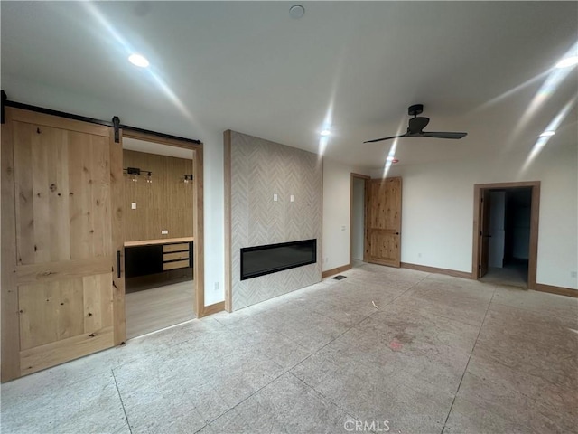 unfurnished living room with a fireplace, a barn door, and ceiling fan