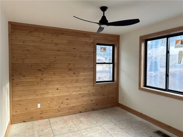 unfurnished room with plenty of natural light, ceiling fan, and wood walls