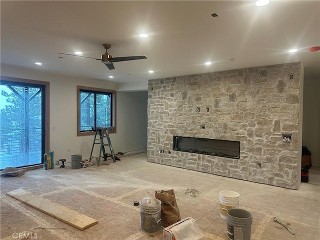 unfurnished living room with ceiling fan and a stone fireplace