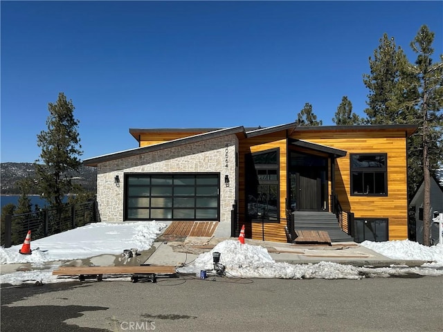 contemporary house featuring an attached garage, stone siding, and fence