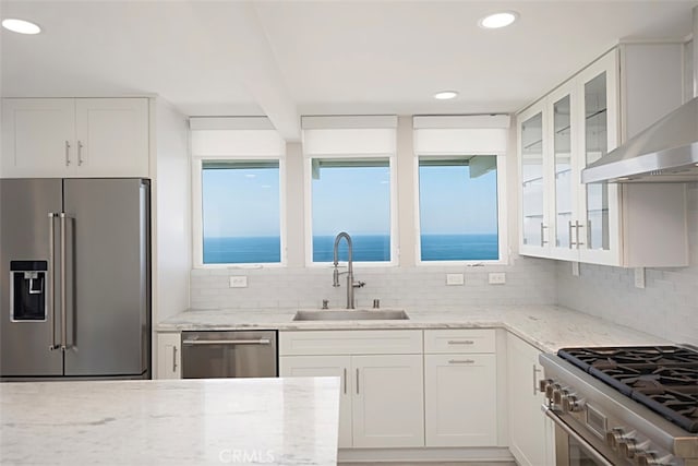 kitchen with white cabinets, wall chimney range hood, backsplash, sink, and high end appliances